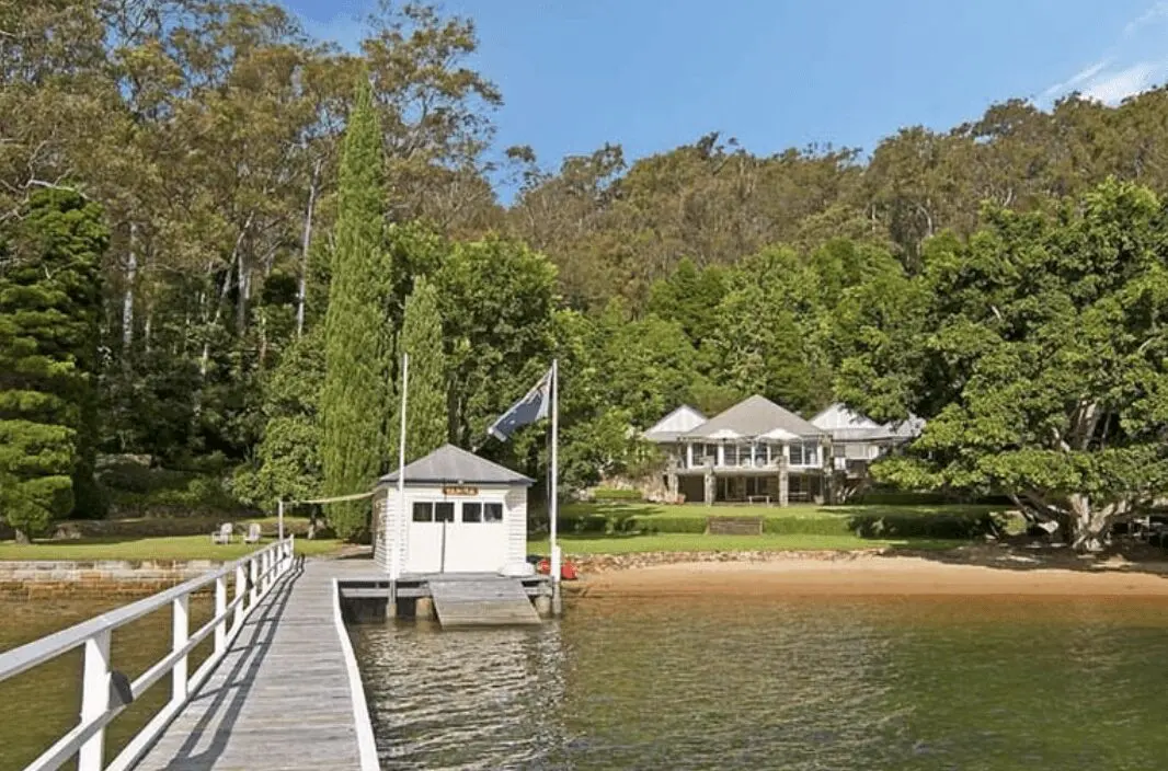 Screenshot 2025-05-06 at 8.45.04 AM View from the end of a private jetty looking back at a peaceful waterfront home and boatshed on Scotland Island, surrounded by lush native trees.
